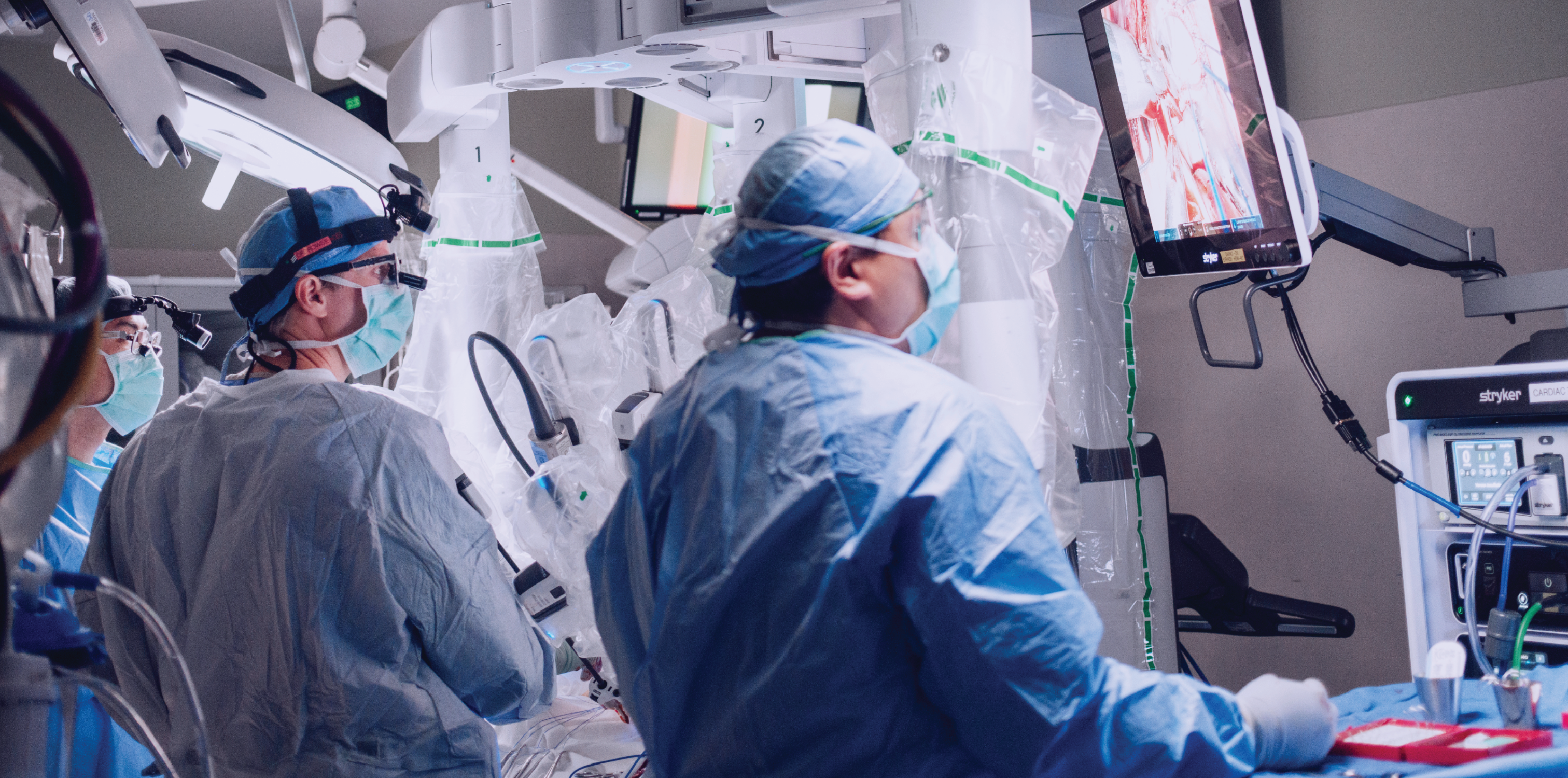Three doctors looking up at monitors for a robotic surgery in an operating room
